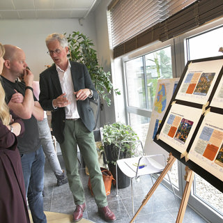Twee medewerkers luisteren naar bestuurder bij bord met poster over gebiedsplannen