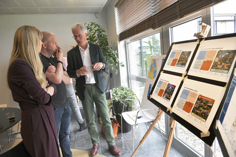 Twee medewerkers luisteren naar bestuurder bij bord met poster over gebiedsplannen